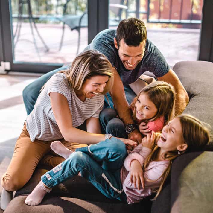 Father and mother tickling children on a couch