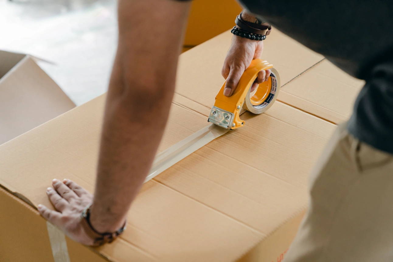 How to pack for a move: a person seals a cardboard moving box securely with packing tape.