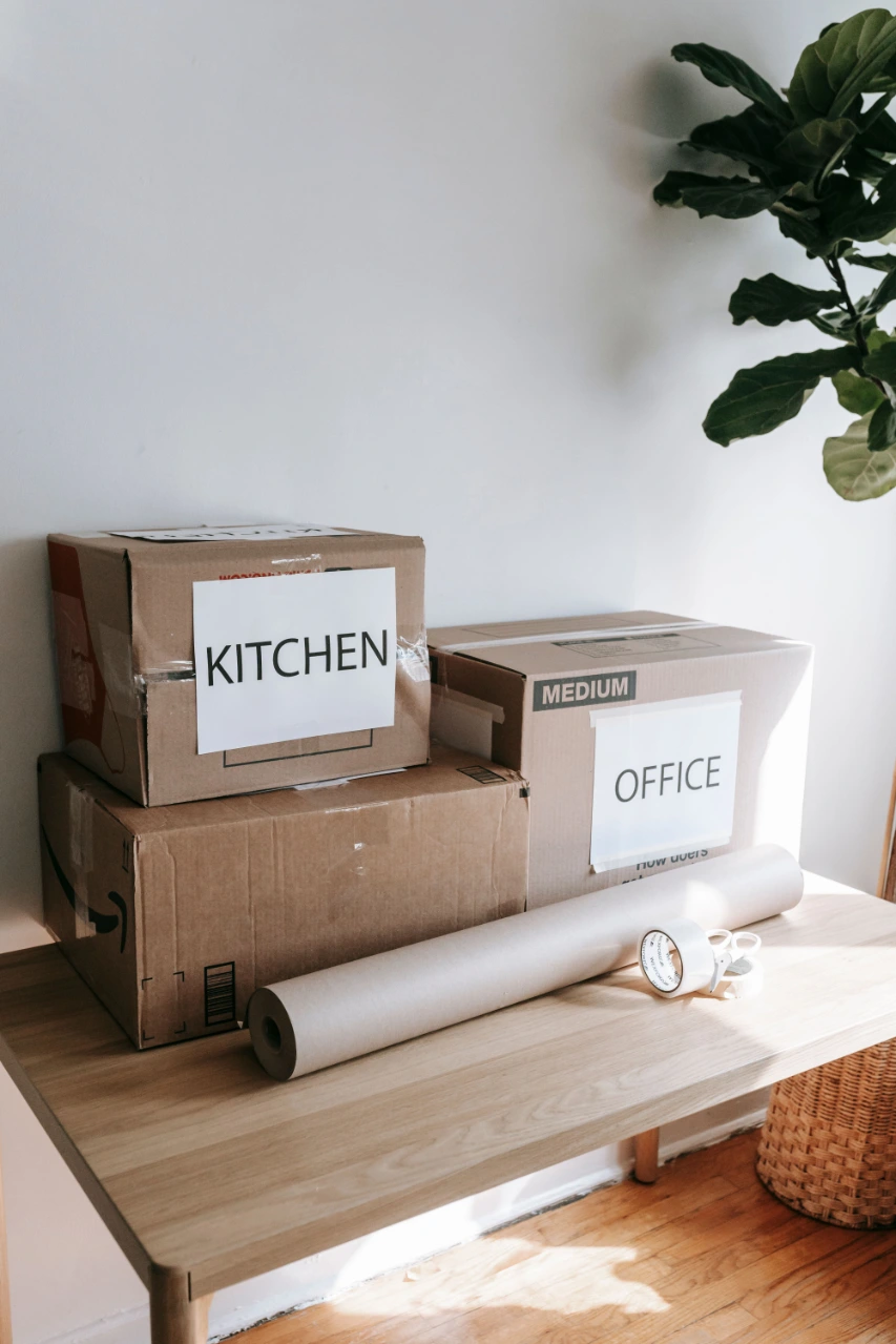 Moving boxes labeled Kitchen and Office beside packing paper, tape, and scissors.