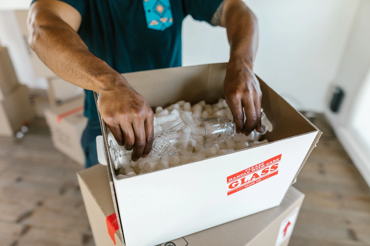 Person placing glassware into a moving box filled with protective cushioning.