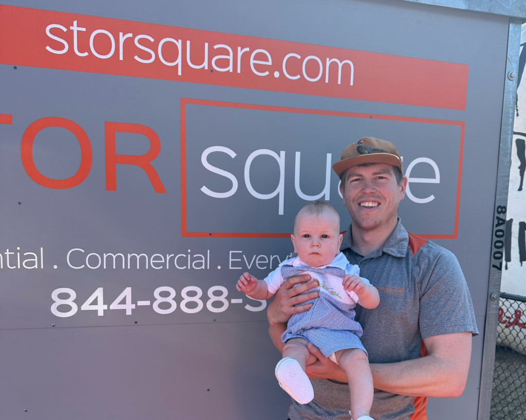 A STORsquare team member smiling while holding a baby in front of a storage container, reflecting the company’s friendly service and customer-focused support.