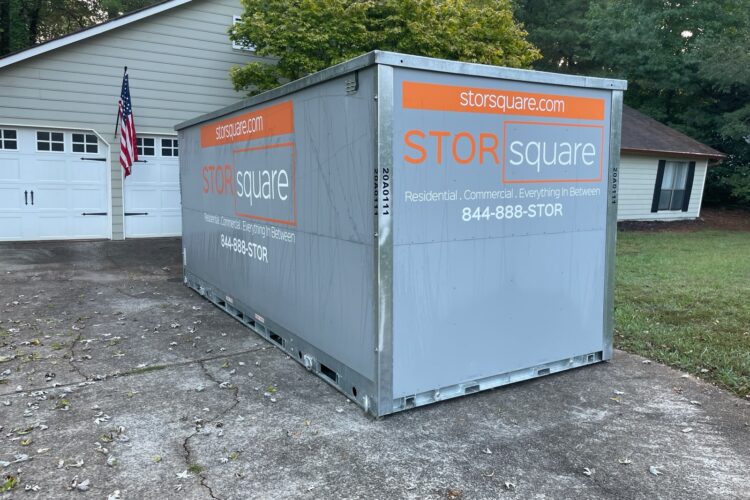 A gray STORSquare mobile unit placed securely on a residential concrete driveway, offering convenient temporary storage solutions during a garage floor coating project.