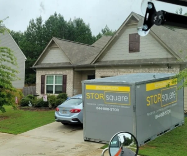Mobile storage units moving are shown in a residential driveway, helping homeowners store belongings while unpacking and preparing for a housewarming party.