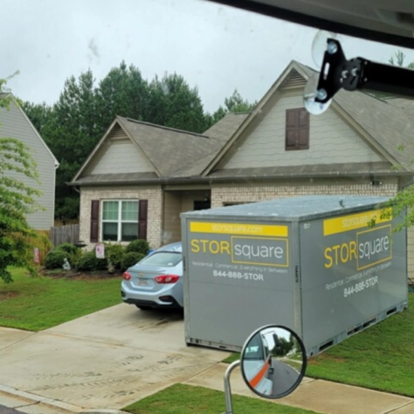 Mobile storage units moving are shown in a residential driveway, helping homeowners store belongings while unpacking and preparing for a housewarming party.