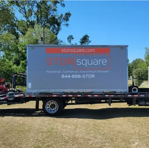 STORsquare flatbed truck transporting a portable storage container across an open grassy area, prepared for delivery in Florida.