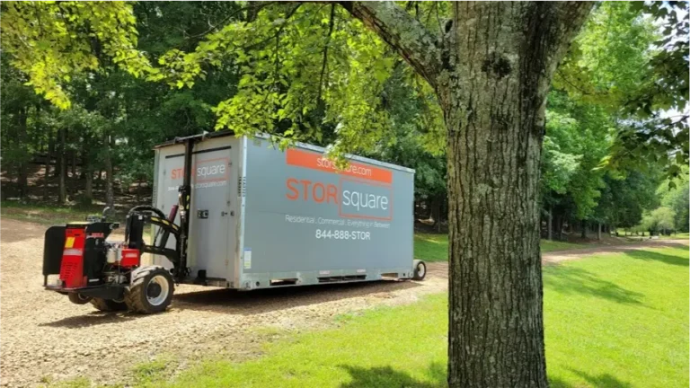 A STORsquare portable storage container placed on a gravel path beside a grassy, wooded property using a no-tilt delivery system.
