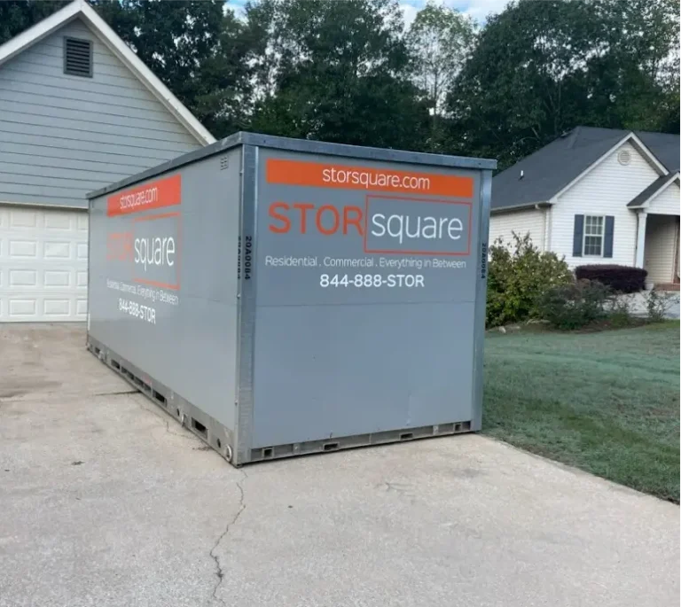 Portable storage container placed in a residential driveway in Alcoa, TN near a light-gray home with attached garage and front lawn.