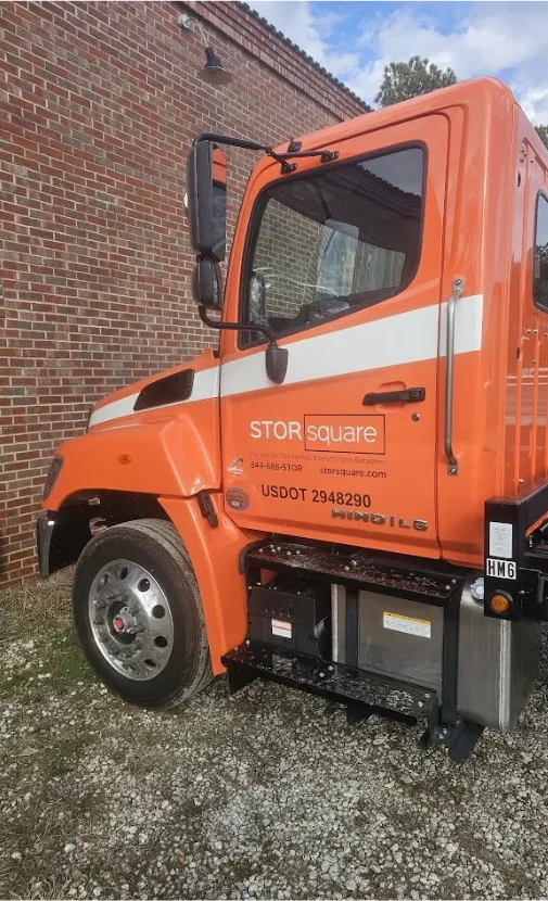 Close-up of a STORsquare flatbed delivery truck cab with branded graphics parked beside a brick building in South Carolina.