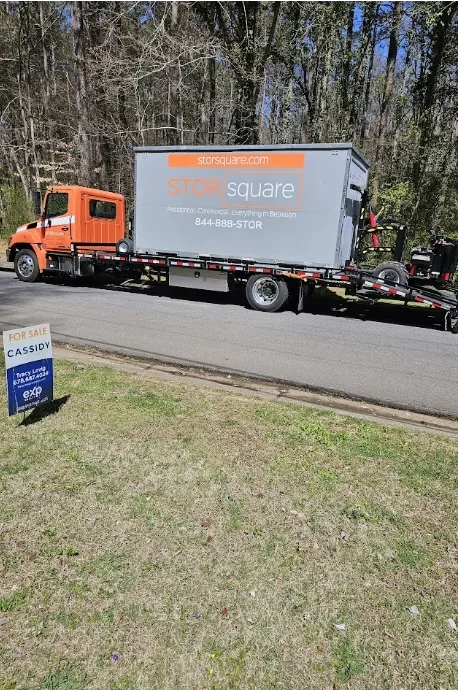 STORsquare flatbed truck transporting a portable storage container along a residential road, prepared for delivery at a North Carolina property.
