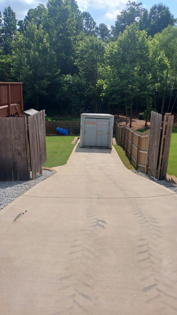 Portable storage container placed down a driveway for organized moving preparation and easy packing access