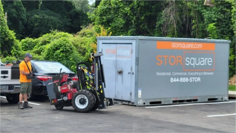 STORsquare moving container being positioned with delivery equipment in Davenport, FL parking area near vehicles and greenery.