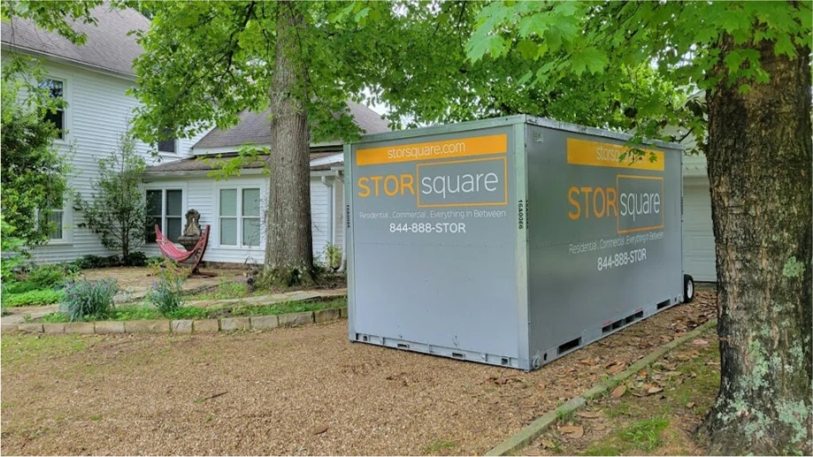 STORsquare portable moving and storage container placed beside a home in Orlando under large trees near a gravel driveway