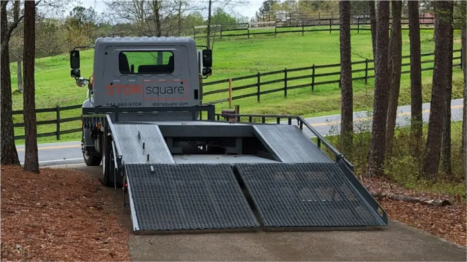 STORsquare delivery truck with ramp lowered on a rural Alvin driveway near a fenced property.
