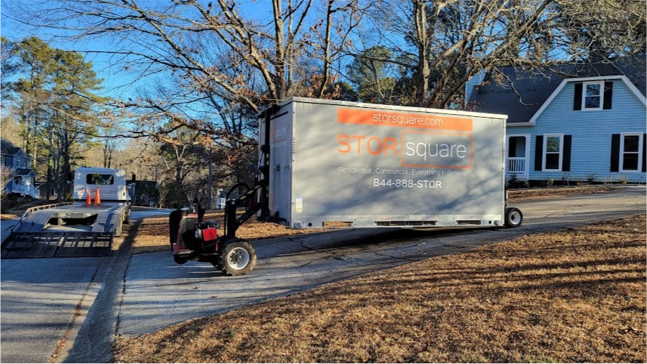 STORsquare portable storage container in Sweetwater being placed on a sloped residential driveway near trees.