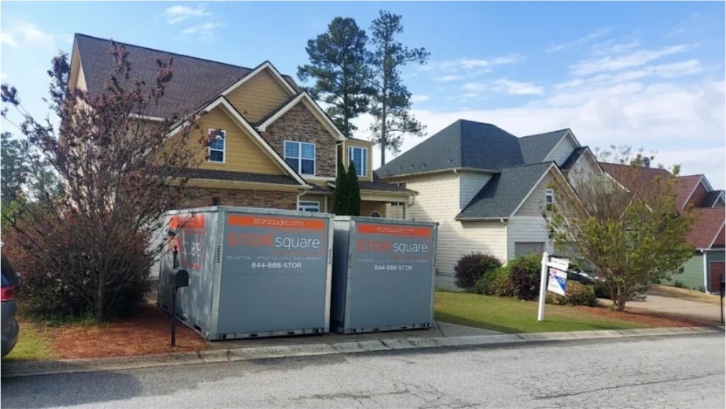 Two STORsquare portable storage containers placed in front of a Cornelia home with a sale sign.