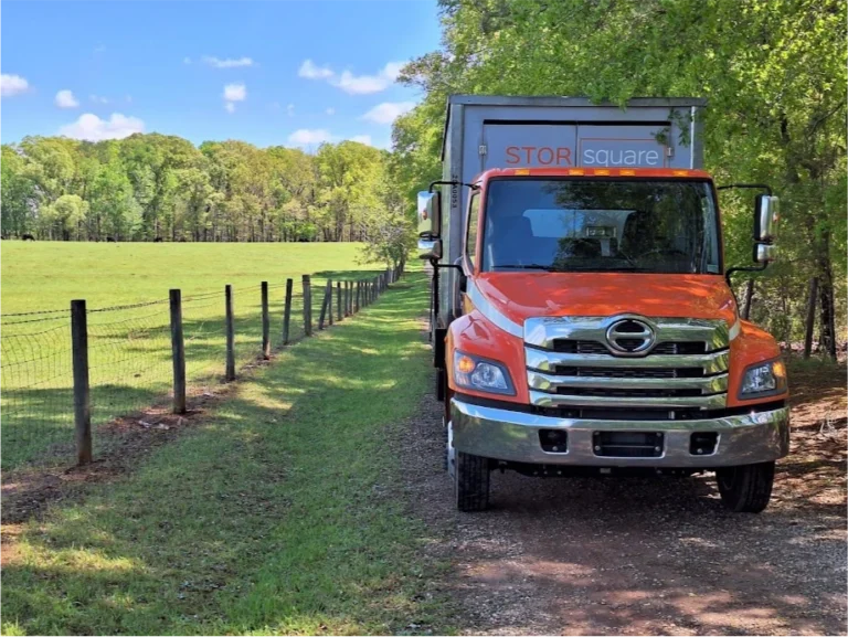 STORsquare delivery truck carrying a portable storage container along a rural driveway in Lexington.