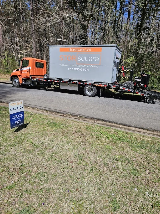 STORsquare truck transporting a portable moving container past a home for sale for customers in Acworth, GA.
