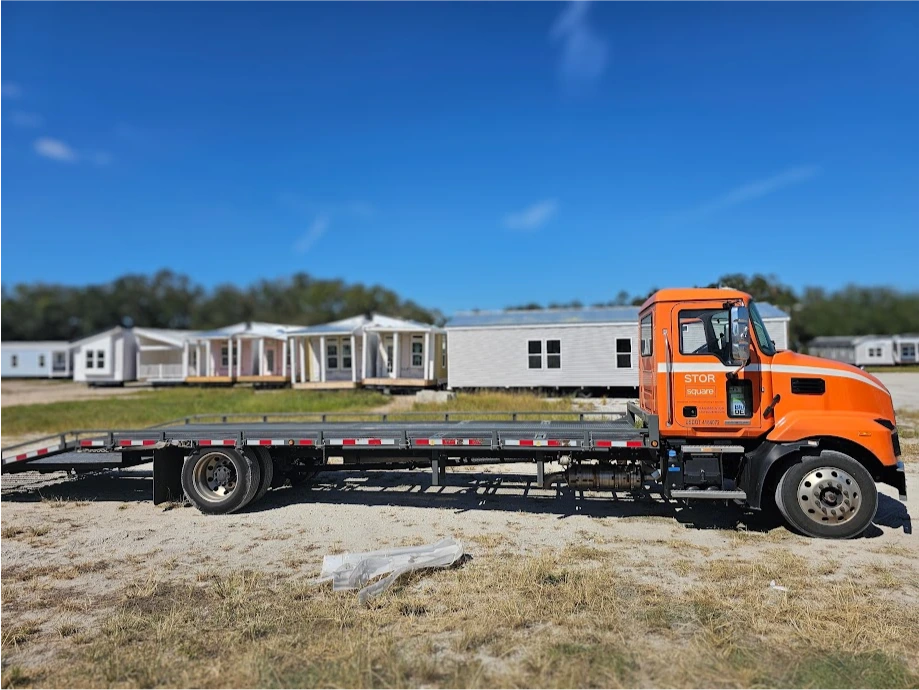 STORsquare flatbed delivery truck parked near manufactured homes for portable storage service in Covington, GA.