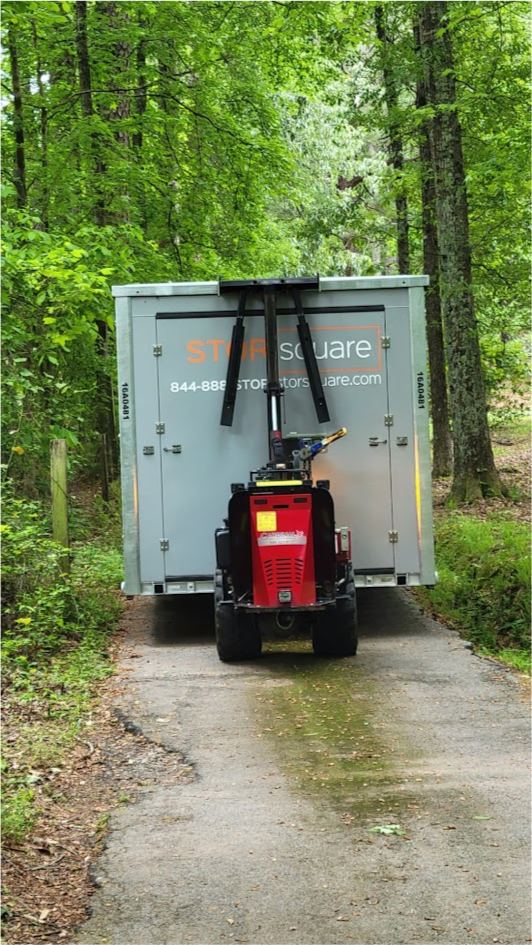 STORsquare portable storage container with placement equipment on a narrow concrete driveway surrounded by tall trees and dense greenery in Brandon, FL.